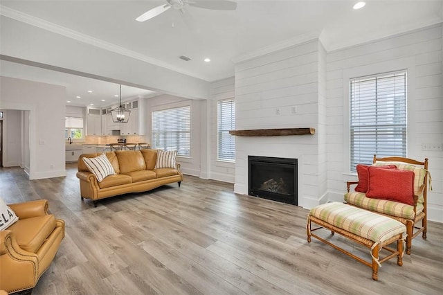 living room with a fireplace, ceiling fan with notable chandelier, light hardwood / wood-style flooring, and crown molding