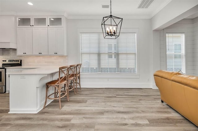 kitchen with white cabinetry, electric range, light hardwood / wood-style floors, decorative light fixtures, and a breakfast bar