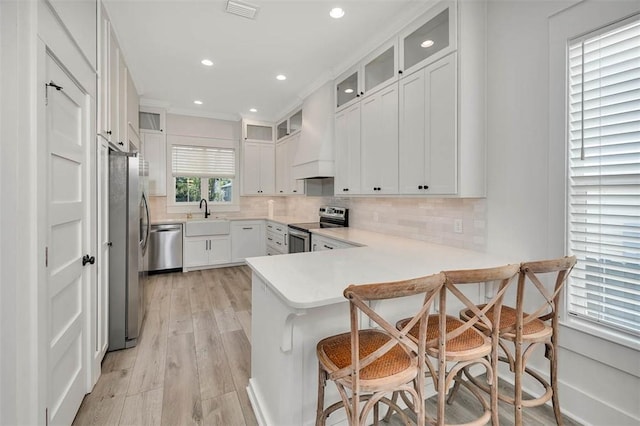 kitchen featuring a kitchen breakfast bar, kitchen peninsula, appliances with stainless steel finishes, white cabinets, and light wood-type flooring