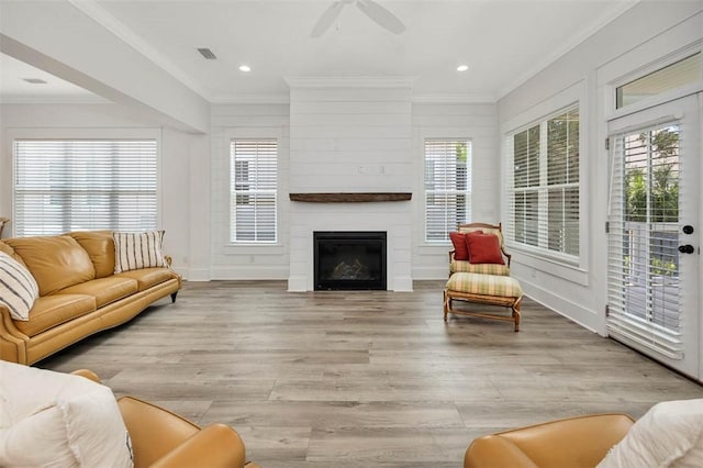 living room with a fireplace, light hardwood / wood-style flooring, ceiling fan, and crown molding