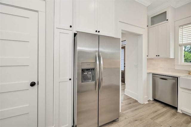 kitchen featuring light wood-type flooring, tasteful backsplash, ornamental molding, stainless steel appliances, and white cabinetry