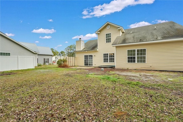 rear view of property featuring a chimney, fence, and a yard