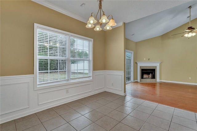 unfurnished dining area with light tile patterned floors, a tile fireplace, ceiling fan with notable chandelier, vaulted ceiling, and wainscoting