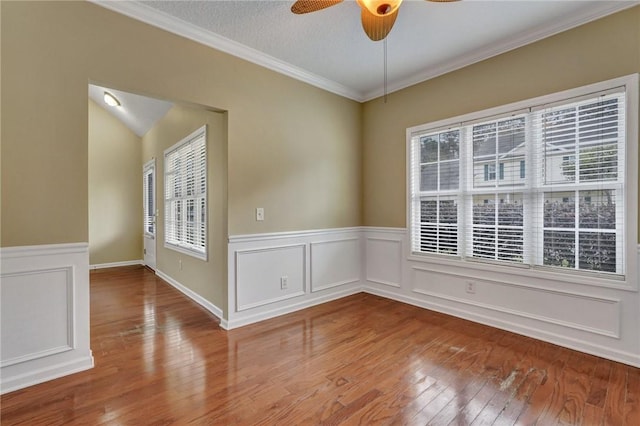 unfurnished room featuring a textured ceiling, a ceiling fan, ornamental molding, wainscoting, and light wood-type flooring