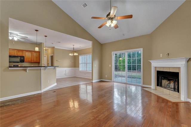 unfurnished living room with visible vents, a tile fireplace, ceiling fan, vaulted ceiling, and light wood-type flooring