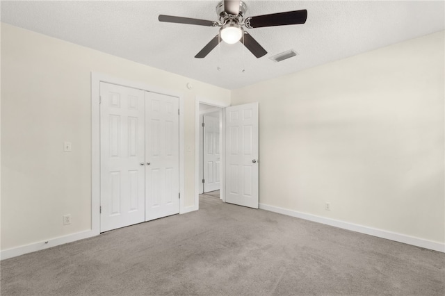 unfurnished bedroom with a textured ceiling, a closet, carpet floors, baseboards, and visible vents