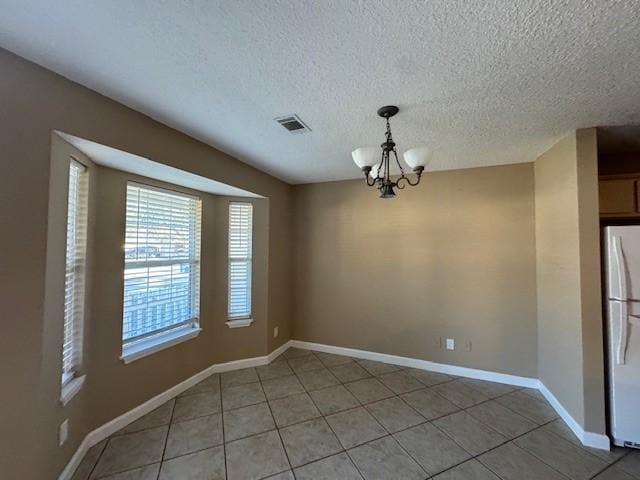 unfurnished dining area featuring tile patterned flooring, a textured ceiling, and an inviting chandelier