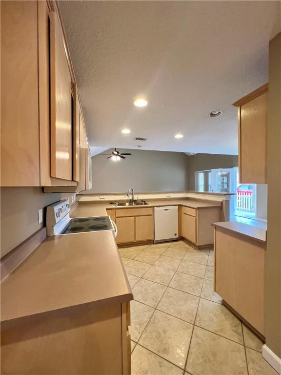 kitchen featuring light brown cabinets, white appliances, vaulted ceiling, light tile patterned floors, and kitchen peninsula