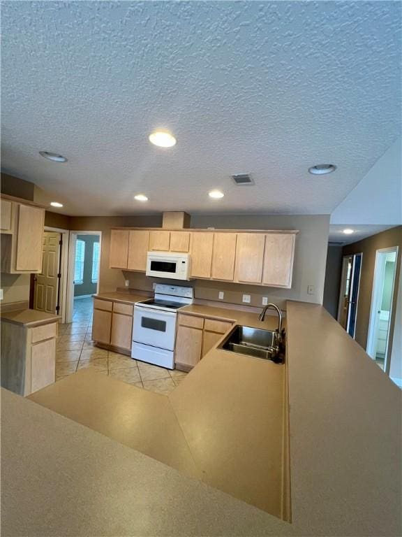 kitchen with a textured ceiling, light brown cabinets, white appliances, and sink