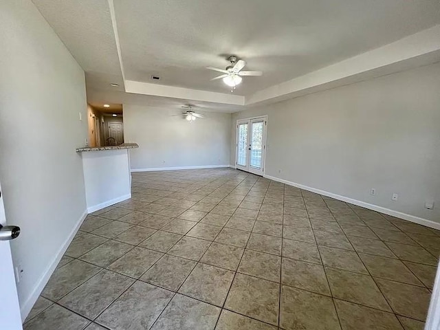 tiled empty room with ceiling fan, a raised ceiling, and french doors