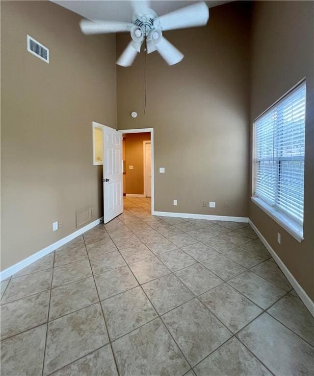 empty room with a high ceiling, light tile patterned floors, and ceiling fan