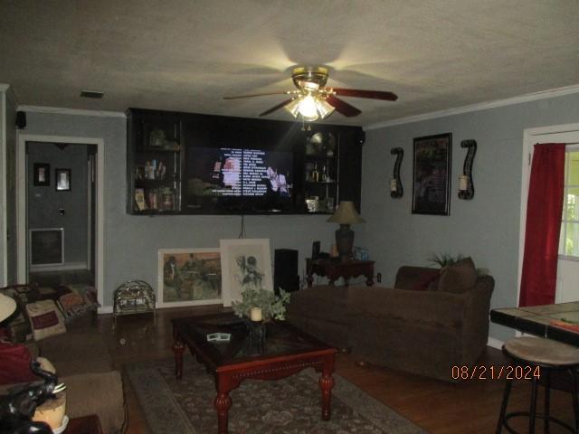 living room with ceiling fan, wood-type flooring, a textured ceiling, and ornamental molding