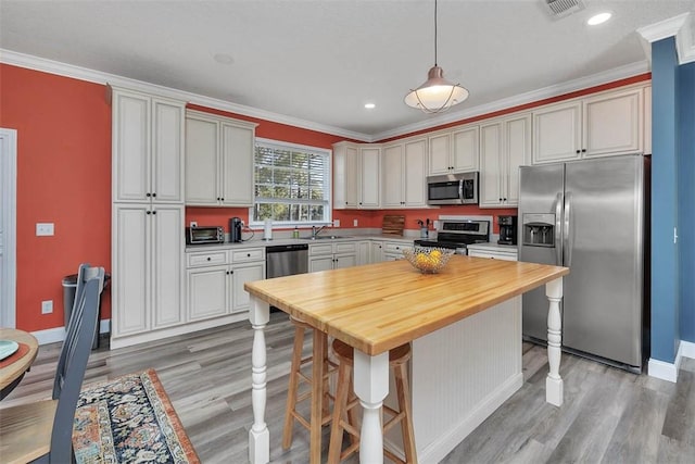 kitchen featuring butcher block countertops, appliances with stainless steel finishes, light wood-type flooring, and ornamental molding