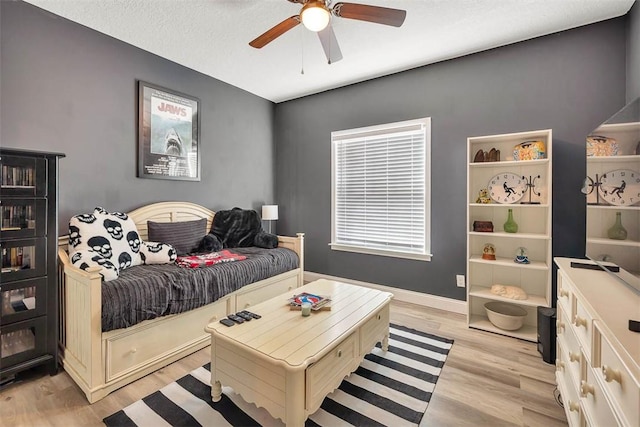 bedroom with light wood-type flooring, baseboards, a textured ceiling, and a ceiling fan