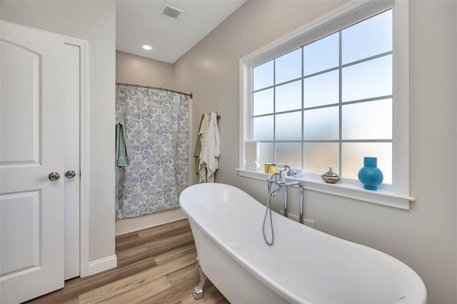 bathroom with a shower with shower curtain, wood finished floors, visible vents, and a freestanding bath