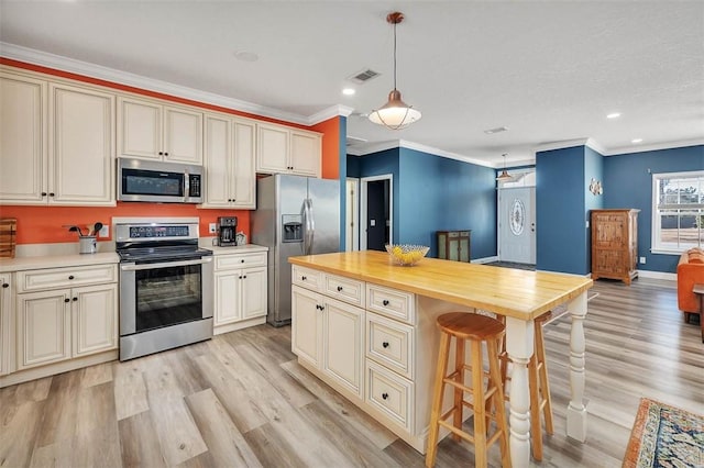 kitchen with light wood finished floors, cream cabinets, stainless steel appliances, and a kitchen bar