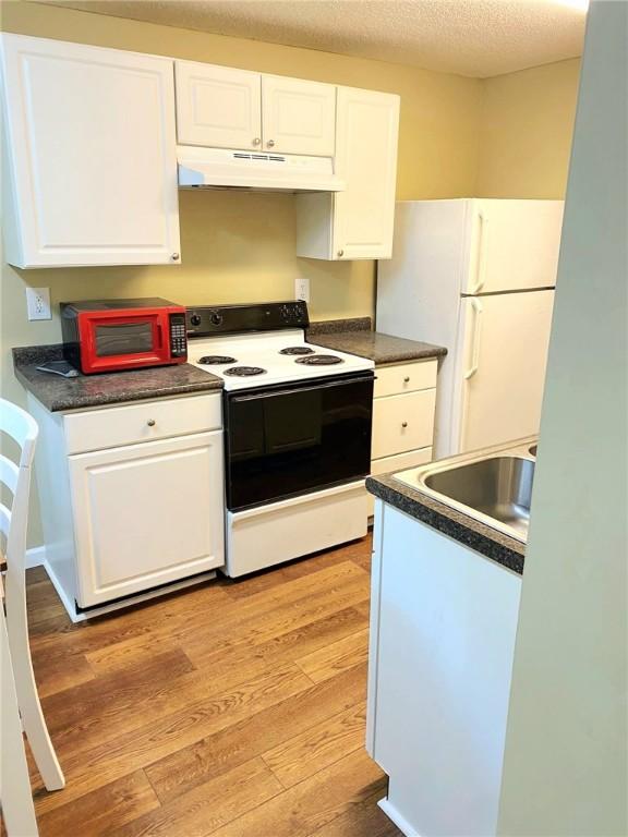 903 Atlantic Ave, Waycross, GA 31501 - kitchen with white appliances, under cabinet range hood, light wood-style flooring, white cabinets, and dark countertops
