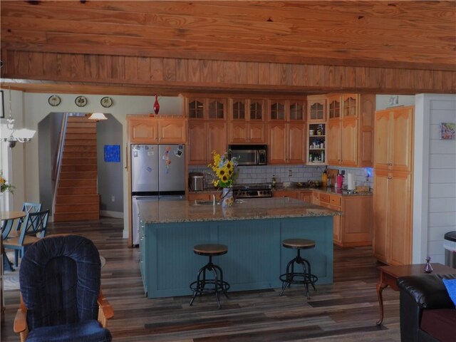 kitchen with a kitchen bar, a center island with sink, decorative backsplash, dark hardwood / wood-style flooring, and stainless steel appliances