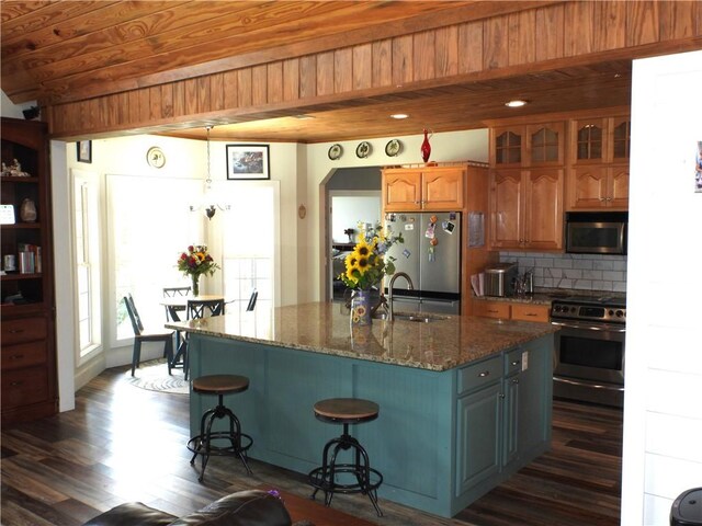 kitchen featuring sink, stainless steel appliances, dark hardwood / wood-style flooring, a center island with sink, and wood ceiling