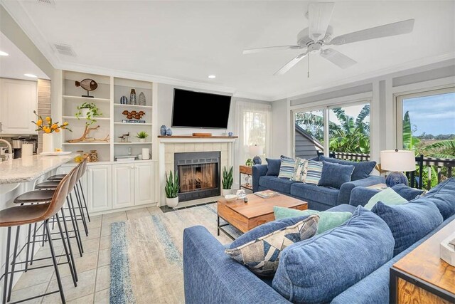 living room featuring ceiling fan, crown molding, light tile patterned floors, built in features, and a fireplace