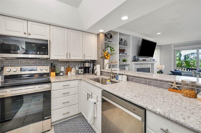 kitchen featuring light stone countertops, white cabinetry, sink, stainless steel appliances, and a fireplace