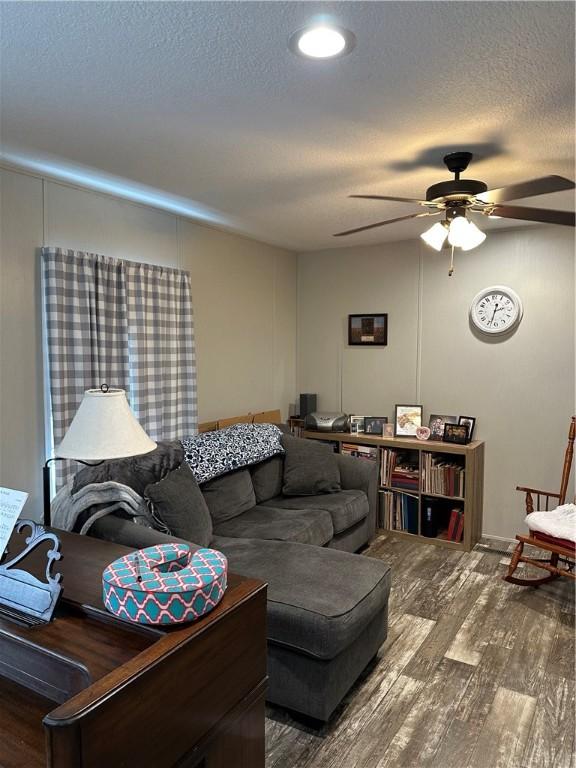 living room featuring hardwood / wood-style flooring, ceiling fan, and a textured ceiling