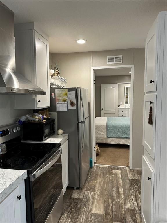 kitchen with white cabinets, appliances with stainless steel finishes, dark hardwood / wood-style flooring, and wall chimney exhaust hood