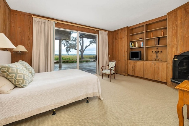 bedroom with access to outside, light colored carpet, a fireplace, and wood walls