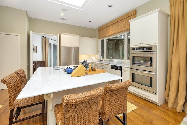 kitchen with a breakfast bar, white cabinetry, a center island, light hardwood / wood-style floors, and stainless steel appliances