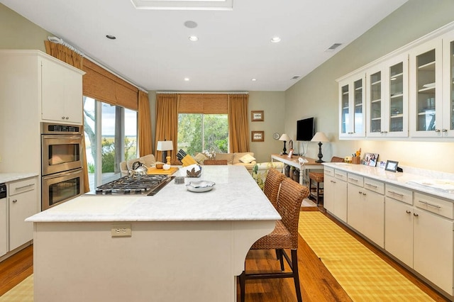 kitchen with light hardwood / wood-style flooring, appliances with stainless steel finishes, a kitchen breakfast bar, a center island, and white cabinets