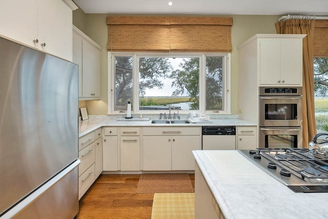 kitchen featuring appliances with stainless steel finishes, sink, white cabinets, and light wood-type flooring