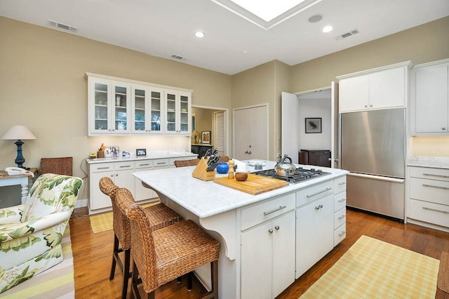 kitchen with appliances with stainless steel finishes, a center island, white cabinets, a kitchen bar, and light wood-type flooring