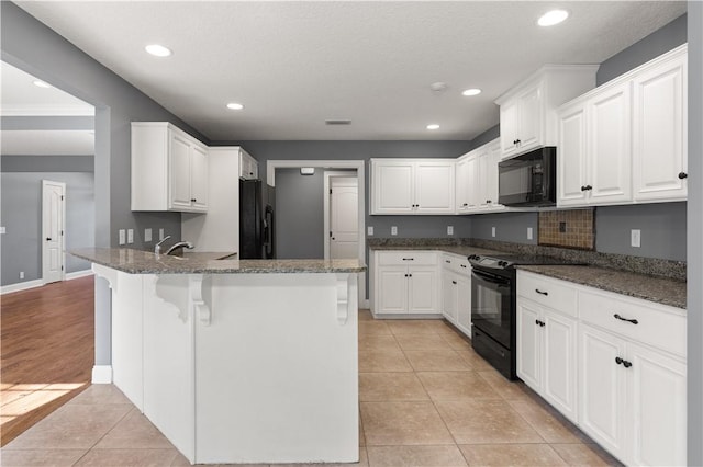 kitchen featuring white cabinets, kitchen peninsula, dark stone countertops, and black appliances