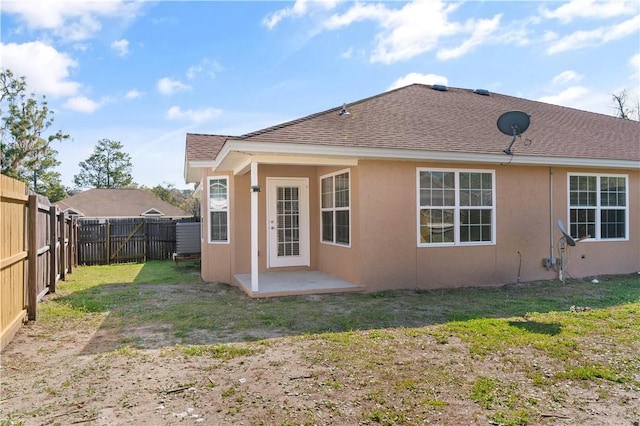 rear view of house with roof with shingles, a yard, a fenced backyard, stucco siding, and a patio area