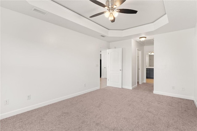 spare room with baseboards, a tray ceiling, light carpet, and visible vents