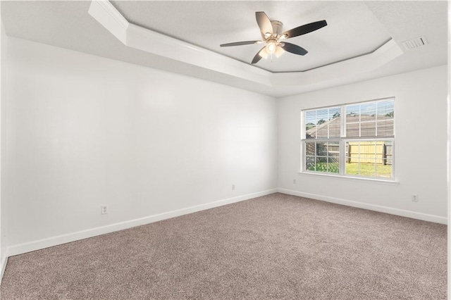 empty room with visible vents, baseboards, carpet floors, a raised ceiling, and a ceiling fan