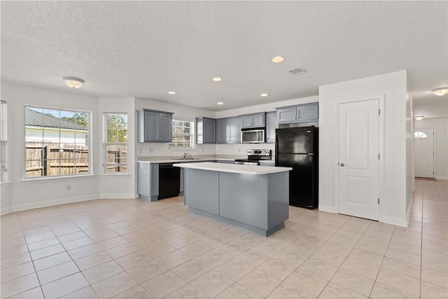 kitchen with black appliances, gray cabinetry, a center island, light tile patterned flooring, and light countertops