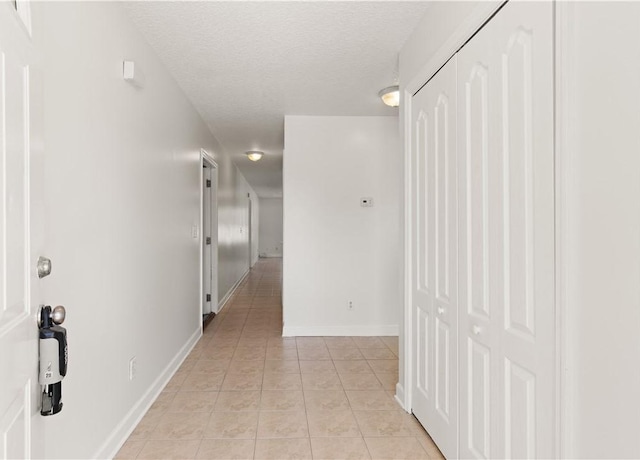 hall featuring light tile patterned floors, a textured ceiling, and baseboards