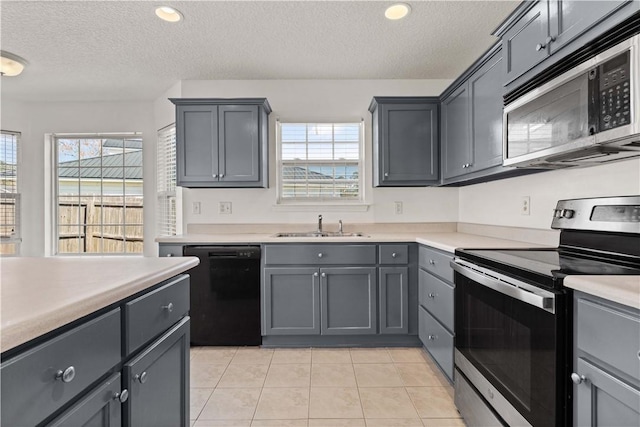 kitchen featuring gray cabinetry, light countertops, light tile patterned flooring, stainless steel appliances, and a sink