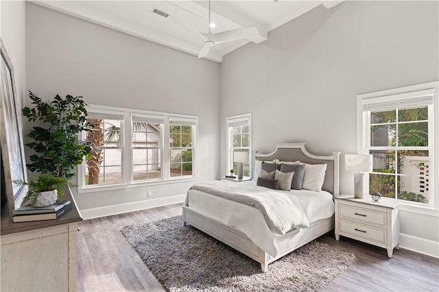 bedroom featuring beam ceiling, wood finished floors, baseboards, visible vents, and a towering ceiling