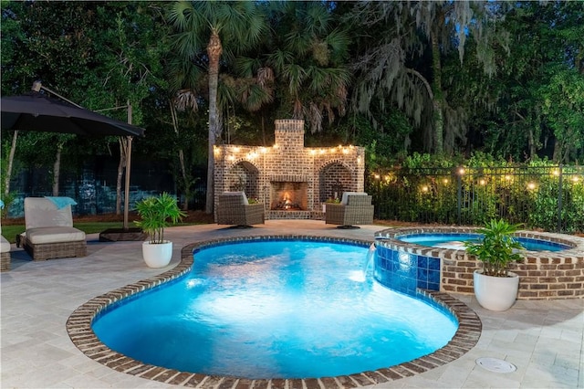 view of pool featuring an outdoor brick fireplace, a pool with connected hot tub, fence, and a patio