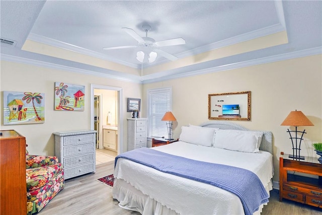 bedroom with visible vents, light wood-style floors, crown molding, and a tray ceiling