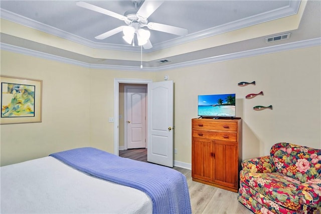 bedroom with crown molding, a tray ceiling, visible vents, and light wood finished floors