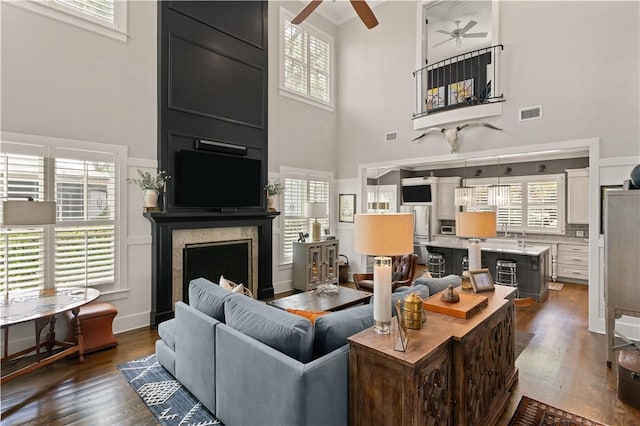 living room with a fireplace, a high ceiling, dark hardwood / wood-style flooring, and ceiling fan