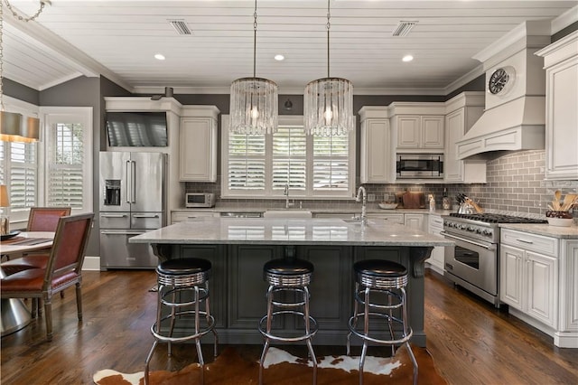 kitchen featuring premium appliances, light stone counters, hanging light fixtures, and a kitchen island with sink