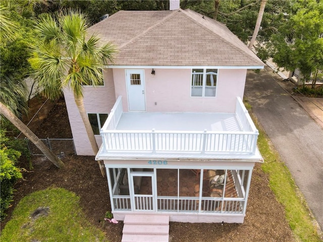 4206 Tenth St, Saint Simons Island, GA 31522 - rear view of house featuring stucco siding, a sunroom, roof with shingles, and a balcony
