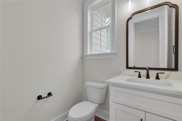 half bath featuring vanity, toilet, and baseboards