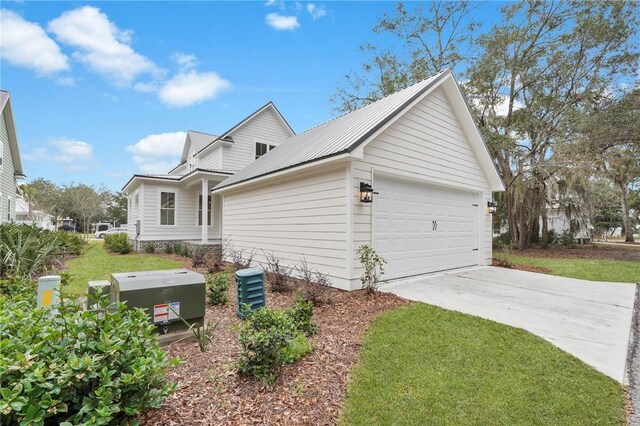 view of side of home with concrete driveway, an attached garage, a lawn, and metal roof