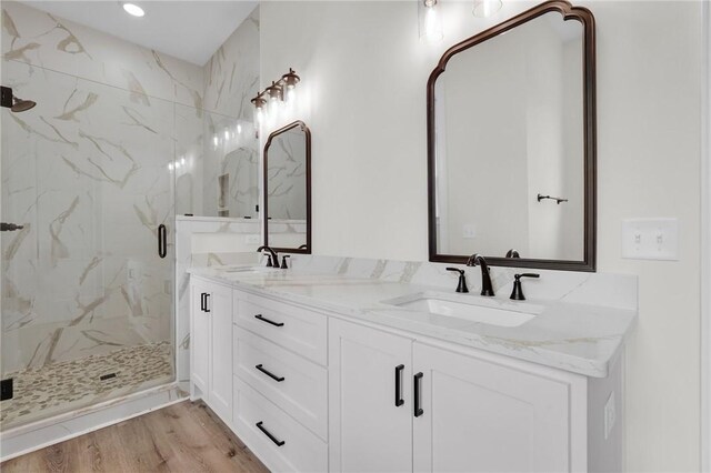 bathroom with a sink, a marble finish shower, wood finished floors, and double vanity