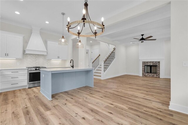 kitchen with premium range hood, a kitchen island with sink, stainless steel electric stove, a fireplace, and decorative backsplash